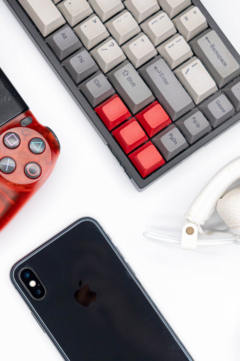 Top view of modern tech gadgets including gaming controller, smartphone, keyboard, and headphones.